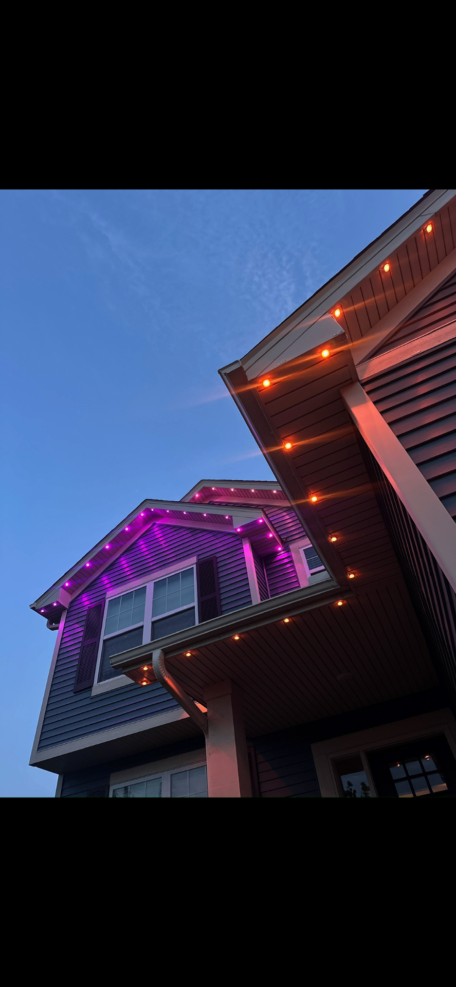 Home eaves with purple and orange permanent LED lights at dusk